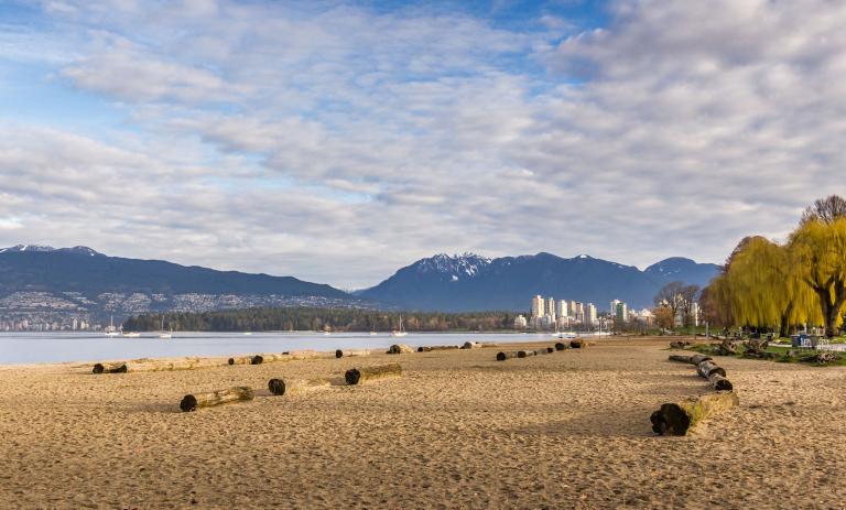 Kitsilano beach with many logs on the sand, with ocean, mountains and downtown vancouver in the background