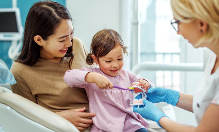 Dentist teaching a little girl how to brush teeth