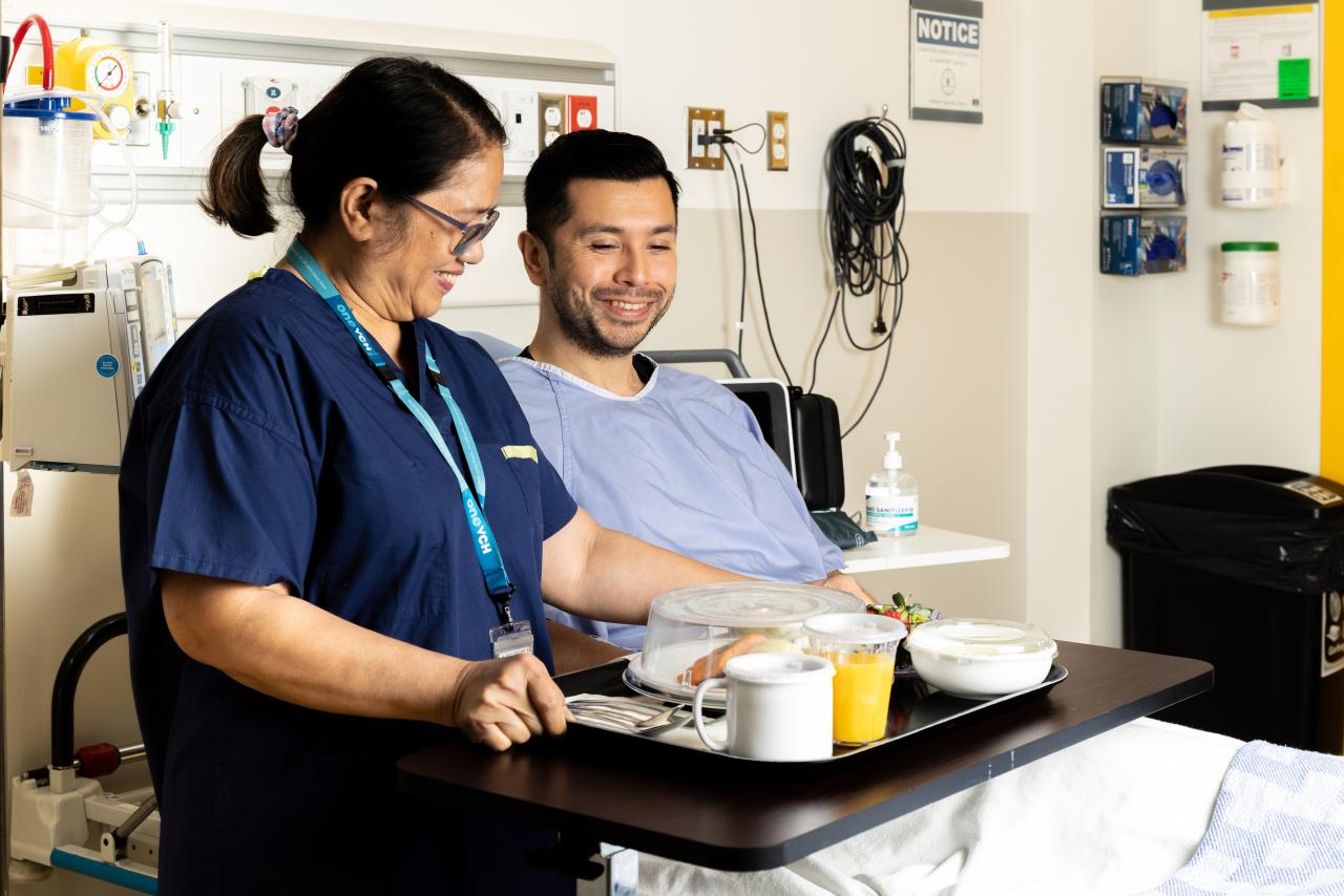 A food service staff member bringing a seated patient their meal in a hospital room.
