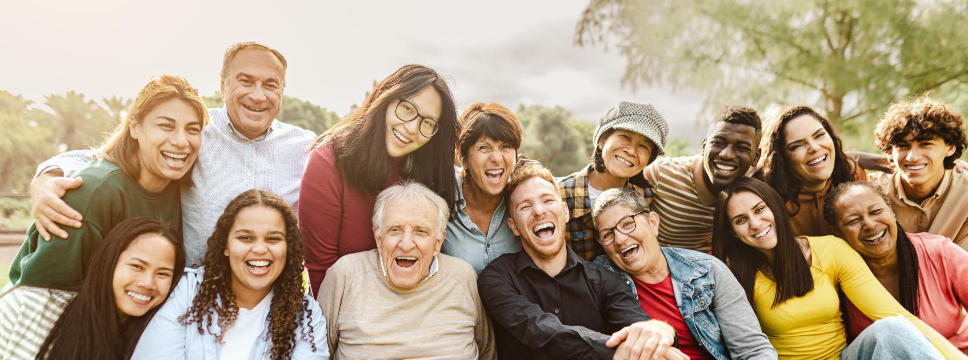 Happy multigenerational people having fun sitting on grass in a public park.