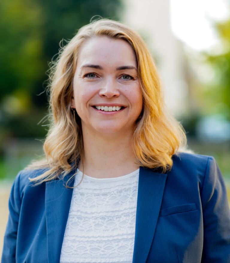 A portrait of Lorraine Blackburn outside on a sunny day. She is wearing a white shirt and blue blazer.