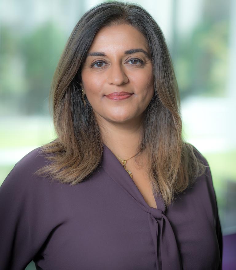 A portrait of Yasmin Jetha indoors. She is wearing a purple shirt