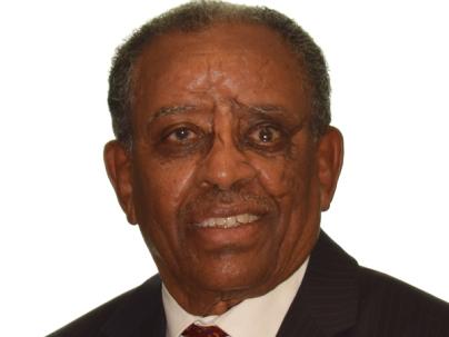 A portrait of Eyob Goitom Naizghi in front of a white background. He is wearing a red tie and dark suit