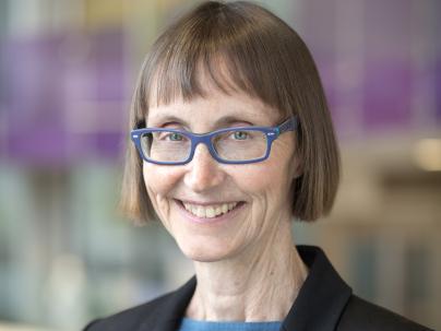 Portrait of Margaret McGregor in front of a colourful background, she is wearing a blue shirt and black blazer